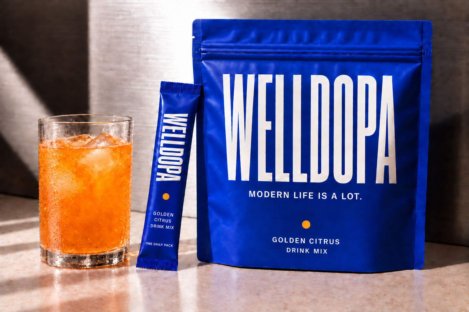 Concept image of the cobalt WellDopa pouch and single-serving stick beside a glass of orange Golden Citrus drink